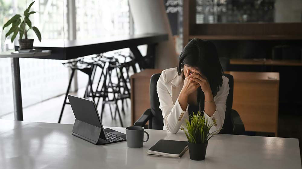 A distressed person sitting at a desk with their head in their hands.